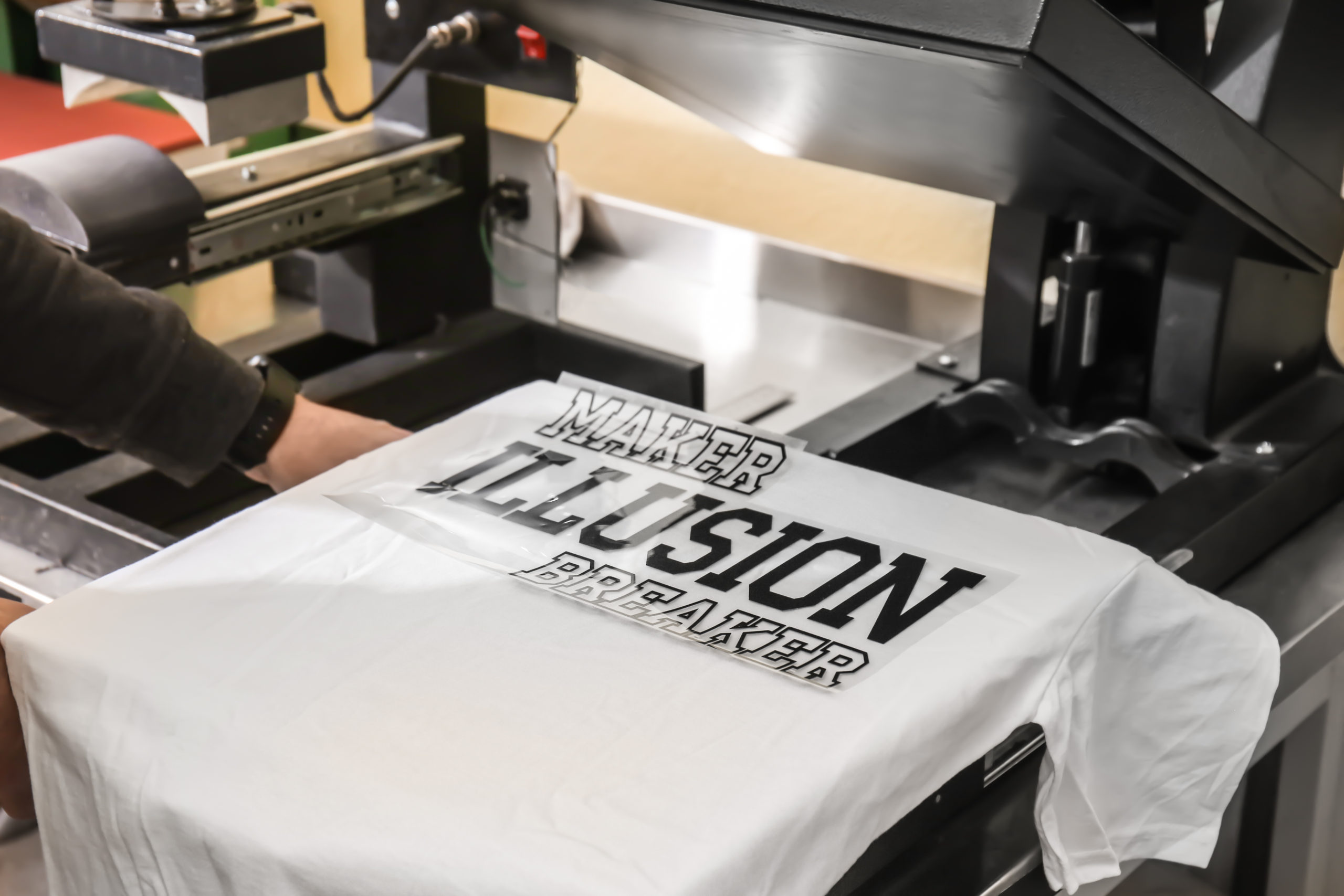 Young man printing on t-shirt at workshop